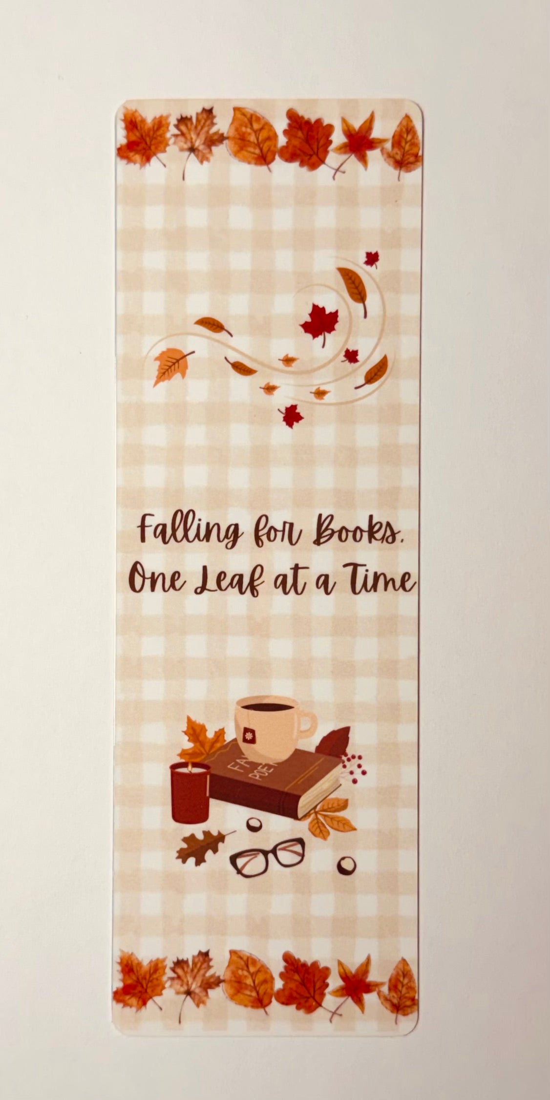 Bookmark with autumn leaves that says "Falling for books. One Leaf at a Time" on a gingham background