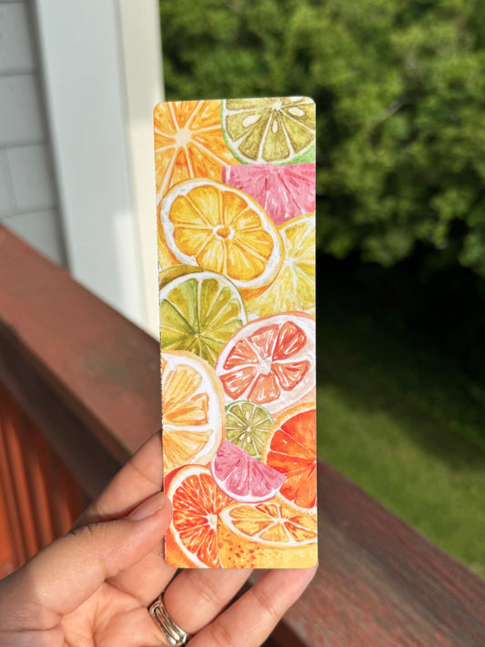 Hand holding a colorful bookmark with citrus fruit design outdoors